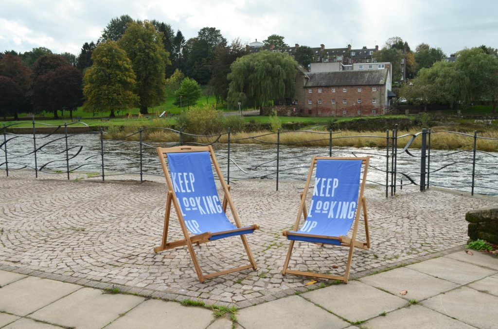 Two blue deckchairs on the banks of the River Nith with 'Keep Looking Up' painted on them 